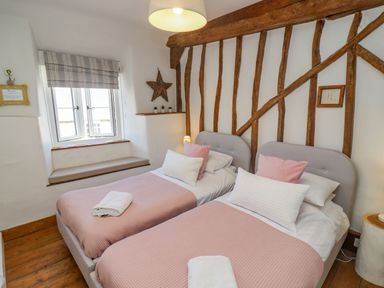 A bedroom with two single beds pink bedding and exposed wooden beams at Chippy Cottage in Chipping Norton