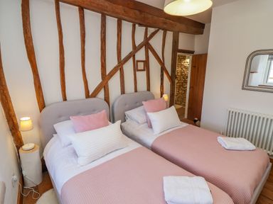 A bedroom with two single beds with pink bedding and pillows next to a wooden beam wall at Chippy Cottage in Chipping Norton