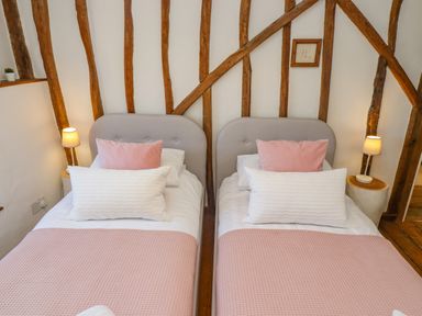 A bedroom with two single beds with pink and white bedding wooden beams on the wall and two bedside lamps at Chippy Cottage in Chipping Norton