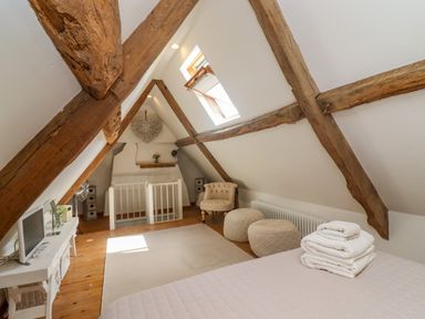 An attic bedroom with exposed wooden beams a bed with folded towels an armchair two round stools a small table with a tv and a skylight at Chippy Cottage in Chipping Norton
