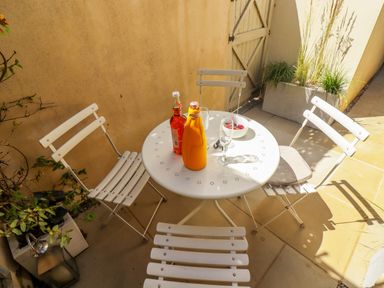 A small outdoor patio area with a round white metal table and four matching chairs with drinks and a bowl on the table at Chippy Cottage in Chipping Norton