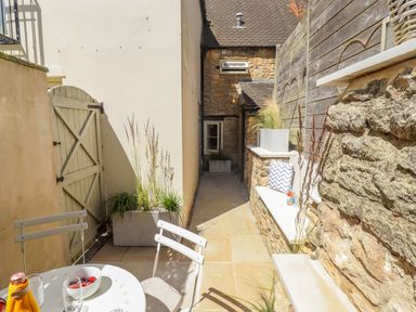 An outdoor patio with a white table and chairs stone walls and planters at Chippy Cottage in Chipping Norton