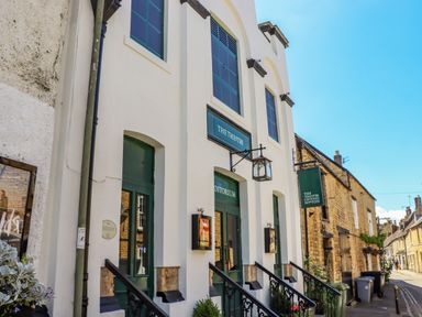 The exterior of a theatre building with green doors and signs on a street with stone buildings at Chippy Cottage in Chipping Norton