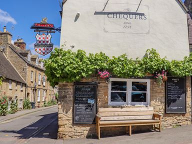 The exterior of The Chequers pub with a bench under a window and plants growing on the wall at Chippy Cottage in Chipping Norton
