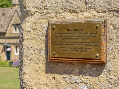 A brass plaque mounted on a stone wall with a house in the background at Chippy Cottage in Chipping Norton