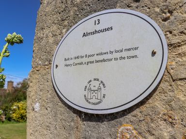 A historical plaque on a stone wall describing almshouses built in 1640 for poor widows in Chipping Norton