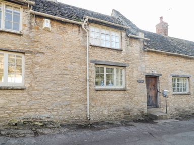 Stone exterior of a house with windows and a wooden door at Holly Cottage in Minster Lovell