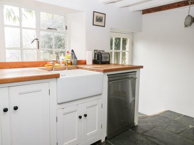 A kitchen with a white farmhouse sink wooden countertops a stainless steel dishwasher and a window at Holly Cottage in Minster Lovell