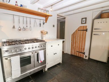A kitchen with a stainless steel stove a hanging utensil rack a small cupboard a wooden door and a cream fridge at Holly Cottage in Minster Lovell