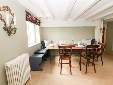 A dining room with a wooden table set with plates and glasses surrounded by wooden chairs and bench seating at Holly Cottage in Minster Lovell