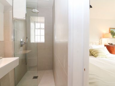 A bathroom with a walk-in shower next to a bedroom with a bed and lamp at Holly Cottage in Minster Lovell