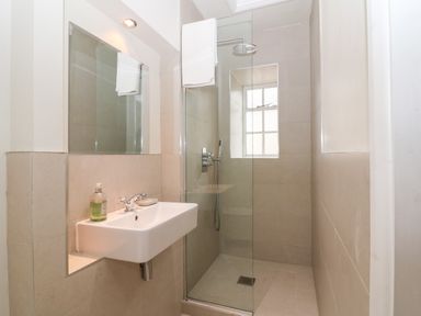A bathroom with a wall-mounted sink and a shower area with glass partition and window at Holly Cottage in Minster Lovell