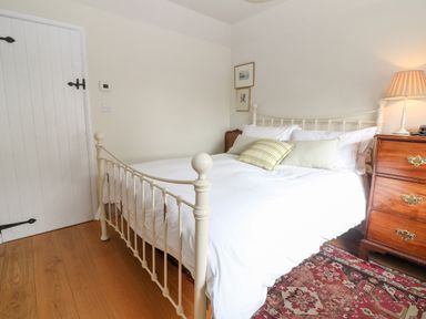 A bedroom with a white metal bed frame wooden dresser lamp and patterned rug at Holly Cottage in Minster Lovell