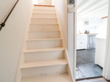 A white staircase next to a kitchen with stone tile flooring and white cabinets at Holly Cottage in Minster Lovell