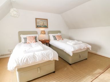 A bedroom with two single beds a wooden nightstand and a painting on the wall at Holly Cottage in Minster Lovell