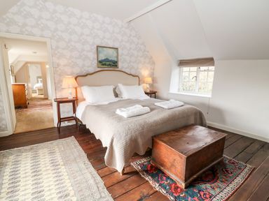 A bedroom with a double bed bedside tables lamps wooden chest and rugs at Holly Cottage in Minster Lovell