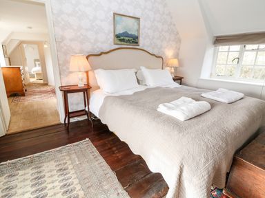 A bedroom with a double bed bedside tables lamps a window and an adjoining room with furniture at Holly Cottage in Minster Lovell