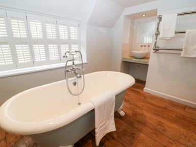A bathroom with a freestanding bathtub wooden floor and a sink with towels at Holly Cottage in Minster Lovell