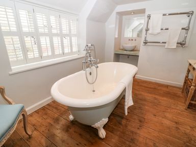A bathroom with a freestanding bathtub on wooden floor near a window with shutters at Holly Cottage in Minster Lovell