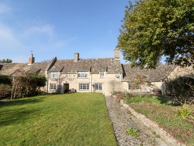 A stone cottage with multiple windows a grassy yard a paved walkway and a tree at Holly Cottage in Minster Lovell
