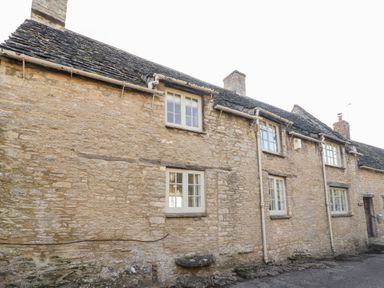 Stone exterior wall of a cottage with multiple windows and a tiled roof at Holly Cottage in Minster Lovell