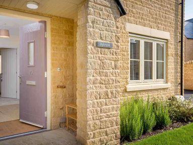An open front door showing part of a stone house with a window and plants at The Bybrook in Bourton-on-the-Water