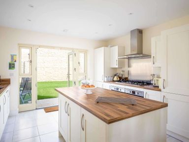 A kitchen with an island wooden countertop and open doors leading to a garden at The Bybrook in Bourton-on-the-Water