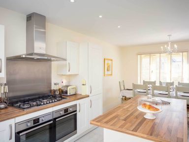 A kitchen with two ovens a gas stove a toaster and a dining table with chairs at The Bybrook in Bourton-on-the-Water