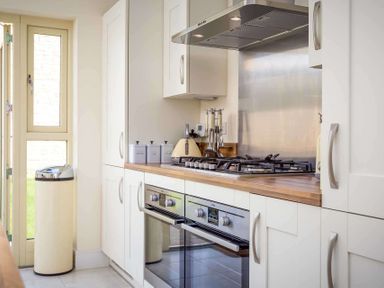 A kitchen with white cabinets a wooden countertop a gas stove double oven and a beige trash can at The Bybrook in Bourton-on-the-Water