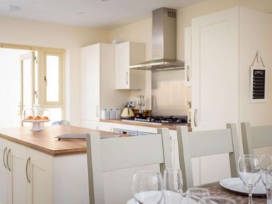 A kitchen with white cabinets a wooden countertop and dining chairs with glasses and plates at The Bybrook in Bourton-on-the-Water