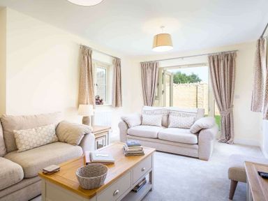 A living room with two beige sofas a wooden coffee table with books and a basket and curtains on windows at The Bybrook in Bourton-on-the-Water