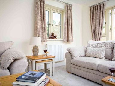 A living room with two beige sofas a wooden coffee table books on the table a lamp and a glass of wine at The Bybrook in Bourton-on-the-Water