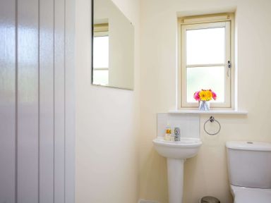 A bathroom with a sink, toilet, towel ring, mirror, window, and flowers on the windowsill at The Bybrook in Bourton-on-the-Water