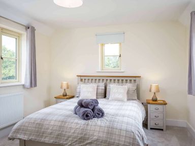 A bedroom with a double bed two bedside tables and two windows at The Bybrook in Bourton-on-the-Water