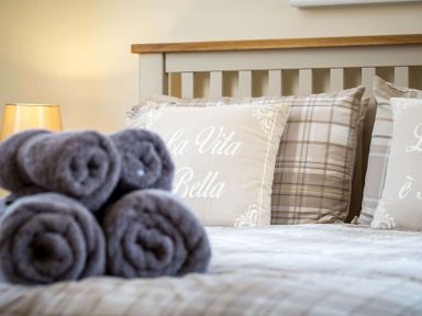 A bed with rolled towels on it and pillows with text on a headboard at The Bybrook in Bourton-on-the-Water