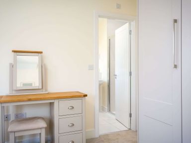 A dressing table with a mirror and stool next to a door leading to a bathroom at The Bybrook in Bourton-on-the-Water