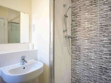 A bathroom with a sink a mirror and a shower area with patterned tiles at The Bybrook in Bourton-on-the-Water