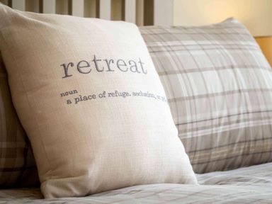 A bedroom with pillows on a bed including one with the word retreat at The Bybrook in Bourton-on-the-Water