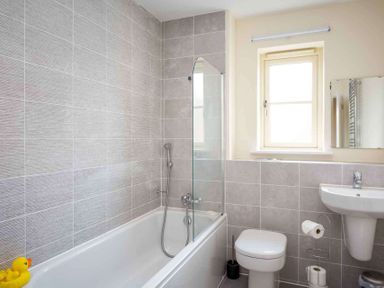 A bathroom with a bathtub a shower a toilet a sink a window and a rubber duck at The Bybrook in Bourton-on-the-Water