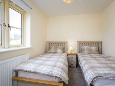 A bedroom with two single beds with plaid bedding a nightstand with a lamp and a window at The Bybrook in Bourton-on-the-Water