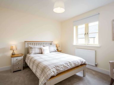 A bedroom with a bed flanked by two bedside tables with lamps and a window at The Bybrook in Bourton-on-the-Water