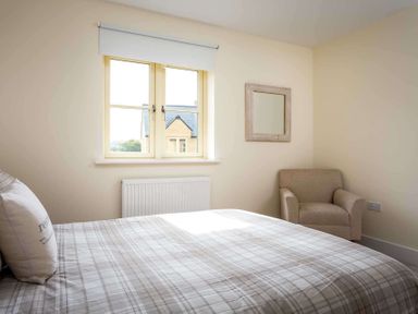 A bedroom with a bed by a window an armchair and a mirror on the wall at The Bybrook in Bourton-on-the-Water