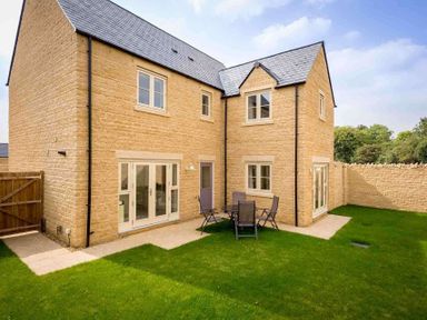 A backyard with a stone house patio table and chairs on the grass at The Bybrook in Bourton-on-the-Water