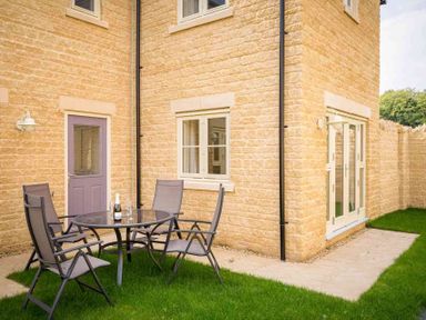 An outdoor patio area with a glass table and four chairs outside a stone house at The Bybrook in Bourton-on-the-Water
