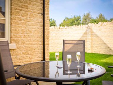 An outdoor patio with a glass round table and three chairs with drinks on the table at The Bybrook in Bourton-on-the-Water