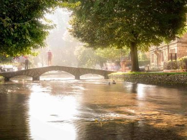 A stone bridge over a river with trees and buildings along the riverbank at The Bybrook in Bourton-on-the-Water