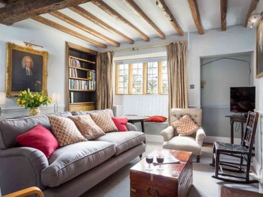 A living room with a gray sofa with cushions a wooden chest a rocking chair and a window seat at Shenley Broadwell