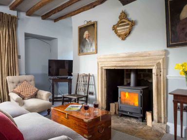 A living room with a wood burning stove in a stone fireplace wooden chest as coffee table sofa armchair and TV at Shenley in Broadwell