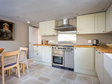 A kitchen with wooden countertops a stainless steel oven and hood a dining table with chairs and a painting on the wall at Shenley in Broadwell