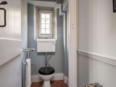 A small bathroom with a toilet having a black seat and a high cistern and a small window above the cistern at Shenley in Broadwell